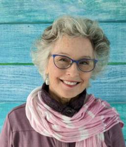 Woman with glasses and scarf in front of blue wall.
